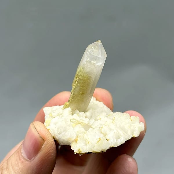 Gradient quartz point standing on white feldspar from Yunxiao, Fujian, China, held in hand