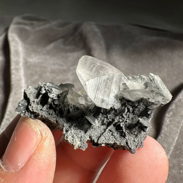 Clear serrated baryte blade on dark calcite from Guangxi, China, held in hand