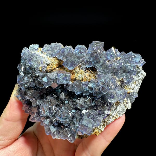Glassy blue-green phantom fluorite cubes with pyrite dust from Fujian, China, held in hand