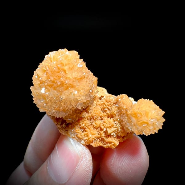 Two peach-orange botryoidal calcite balls from Yunnan, China, held in hand