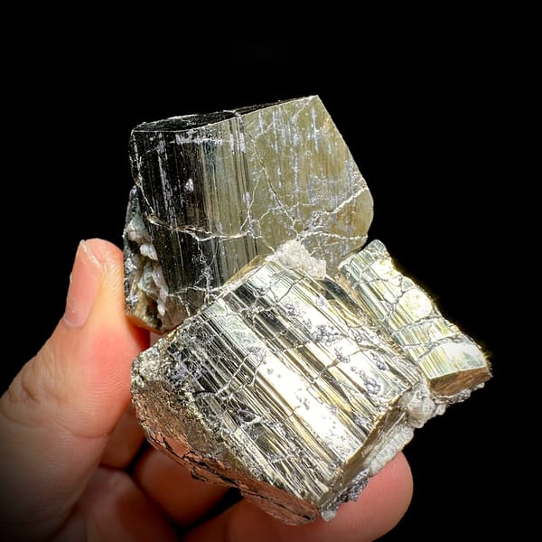 Two interlocking striated brass-gold pyrite crystals from Hunan, China, held in hand