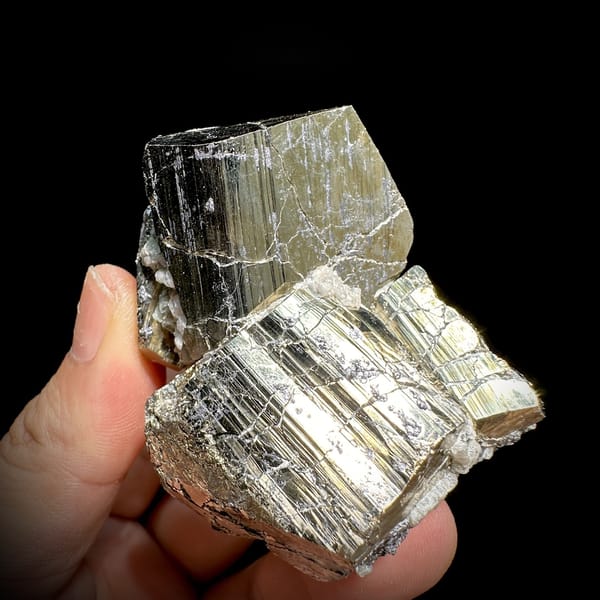 Two interlocking striated brass-gold pyrite crystals from Hunan, China, detail of the matrix contact