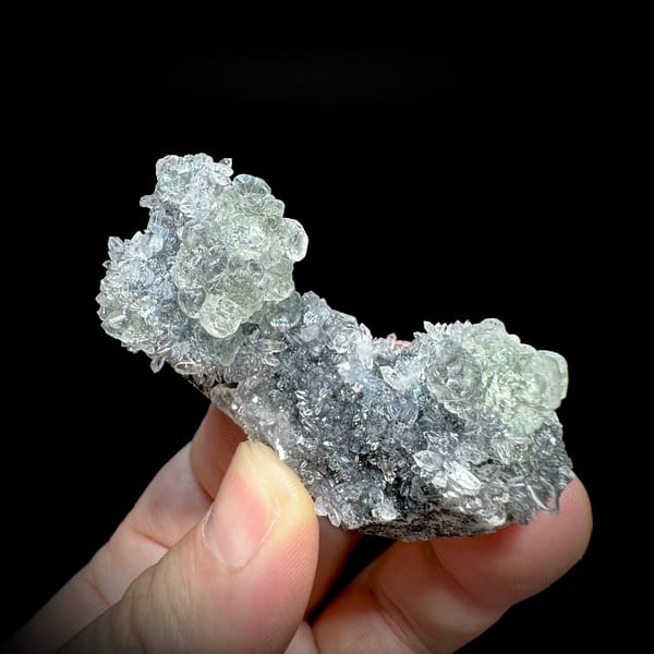 Pale green stepped fluorite on dark quartz druse from Fujian, China, held in hand