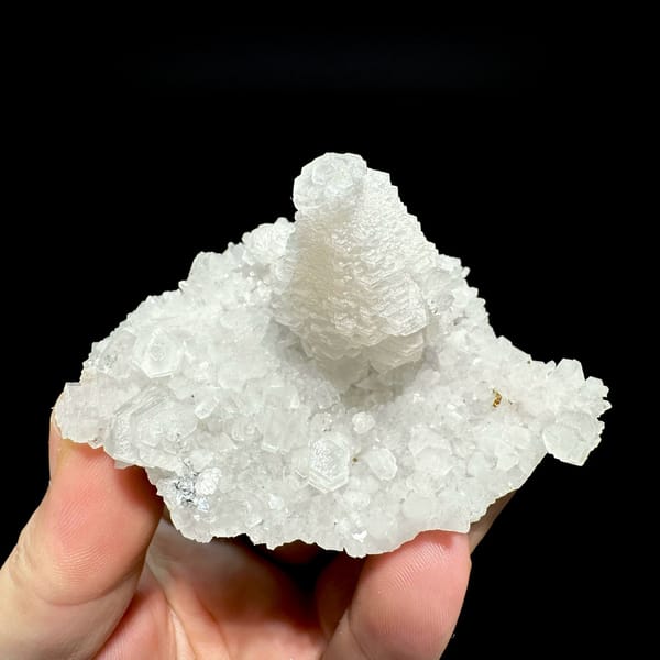 White pagoda calcite tower on quartz druse from Guangdong, China, held in hand