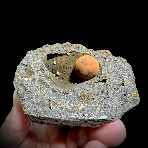 Football-shaped orange calcite ball in grey rock pocket from Fujian, China, close-up of the crystal faces