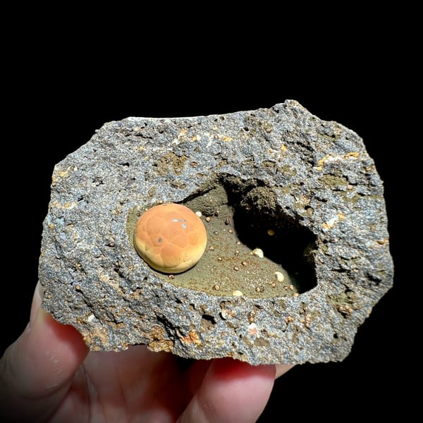 Football-shaped orange calcite ball in grey rock pocket from Fujian, China, top view