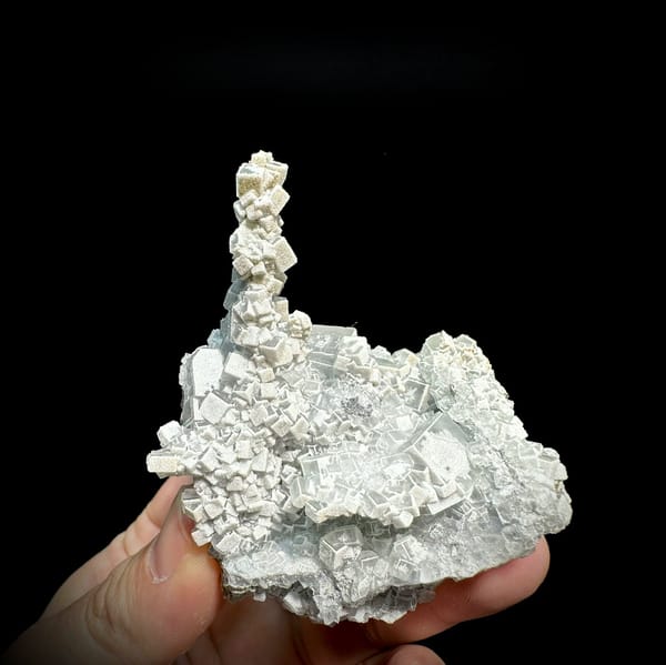 Sketch-patterned fluorite pillar of stacked cubes from Fujian, China, held in hand