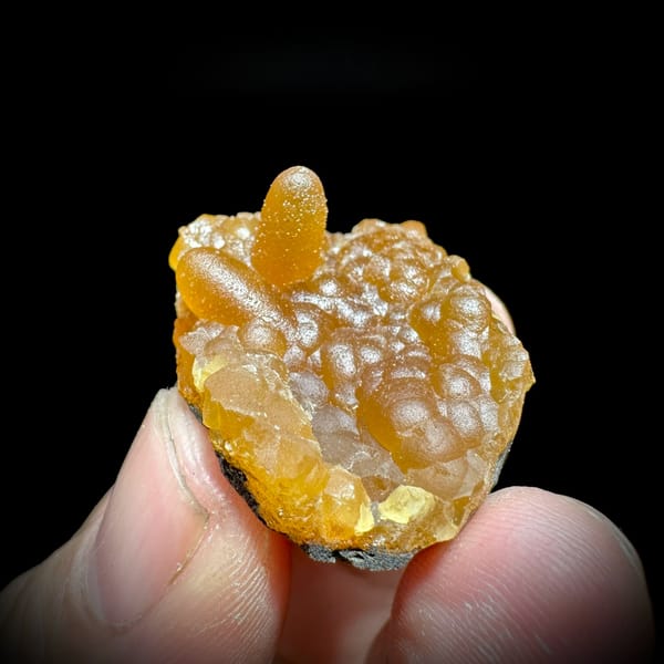 Tiny orange caterpillar-form calcite from Yunxiao, Fujian, China, held in hand