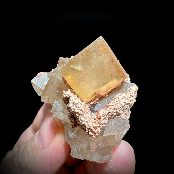 Honey-yellow fluorite cube on pink baryte and calcite from Beijing, China, held in hand