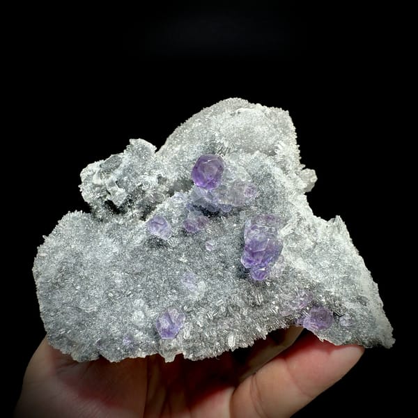 Purple fluorite octahedra on grey quartz mound from Fujian, China, held in hand