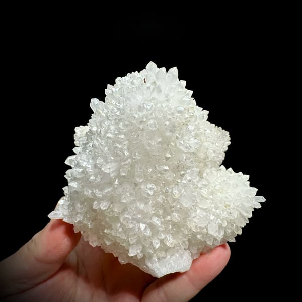 Hollow-shell quartz cluster covered in white points from Fujian, China, held in hand