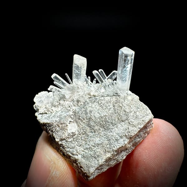 Long transparent aurora calcite prisms on grey rock from Zhejiang, China, held in hand