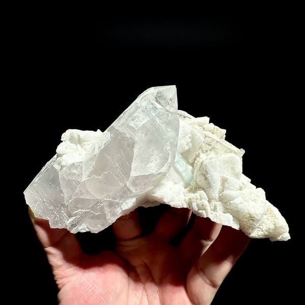 Pale aquamarine prism crossing clear quartz on feldspar from Pakistan, held in hand