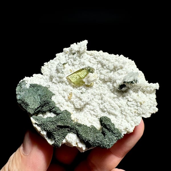 Yellow-green titanite crystal on white druse with chlorite from Pakistan, held in hand