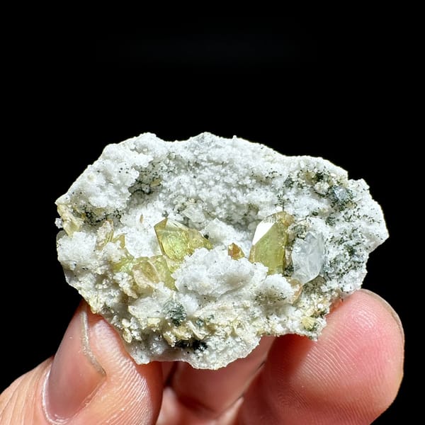 Yellow-green titanite crystals in white feldspar pocket from Pakistan, held in hand