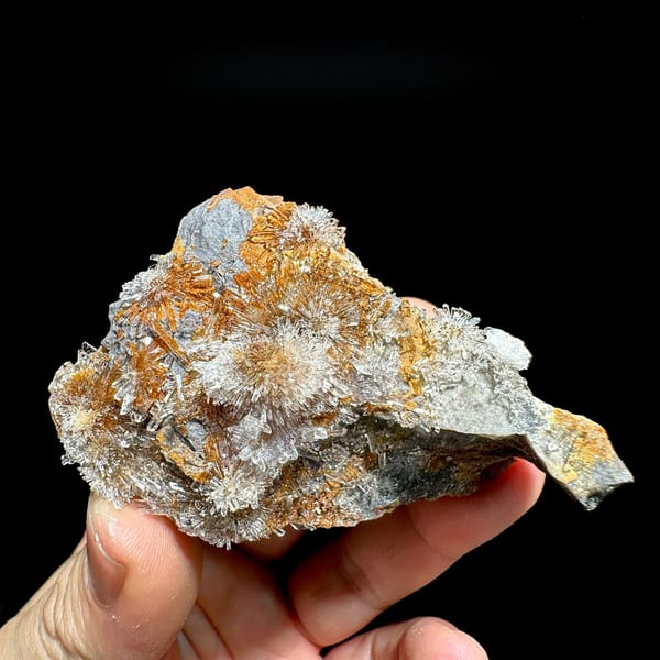 Transparent creedite flower sprays on rust-orange matrix from Guizhou, China, held in hand