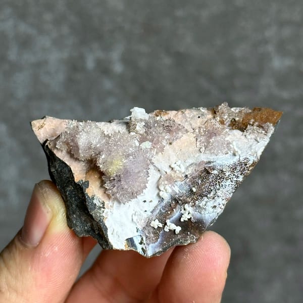 Purple and yellow creedite balls on grey matrix from Guizhou, China, held in hand