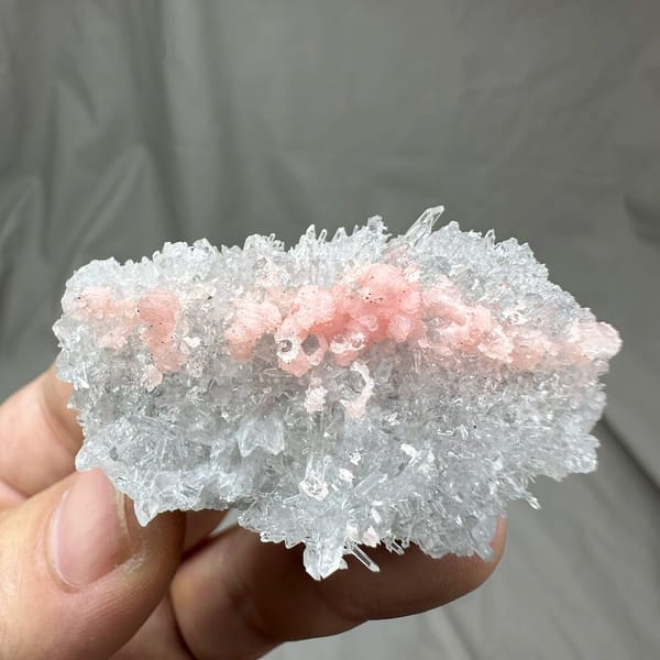 Band of pink rhodochrosite through white quartz needles from Guangxi, China, held in hand