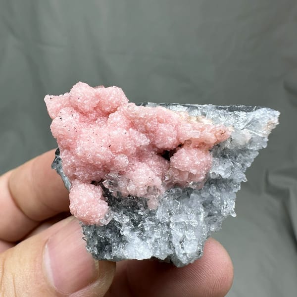 Rose-pink rhodochrosite over grey quartz with pyrite from Guangxi, China, held in hand