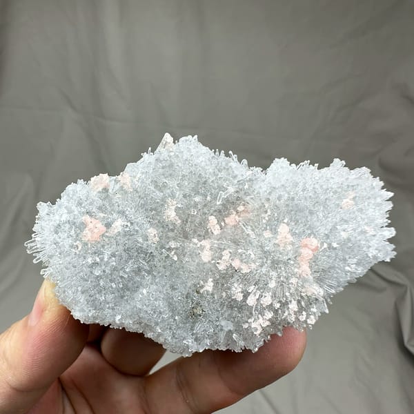 Pink rhodochrosite flecks in frosted white quartz cluster from Guangxi, China, held in hand