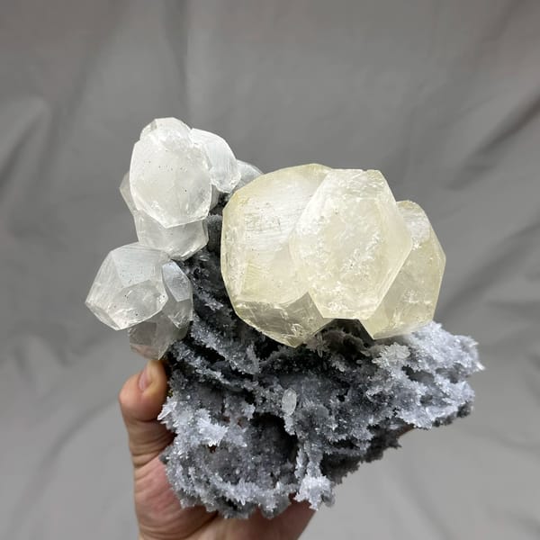 Large yellow-tinted calcite crystal on grey quartz from Fujian, China, held in hand