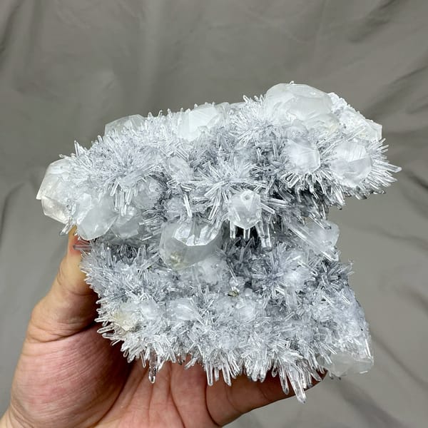 Frosted quartz needles around pale calcite prisms from Fujian, China, held in hand