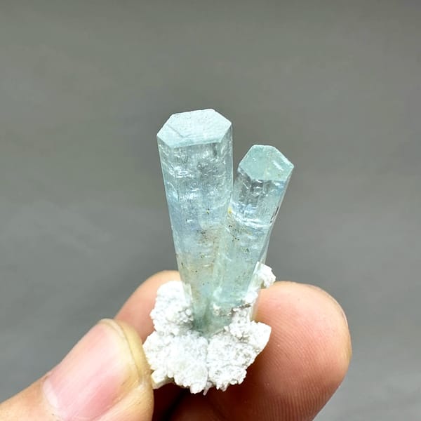 Two sea-blue aquamarine prisms on white feldspar from Namibia, held in hand
