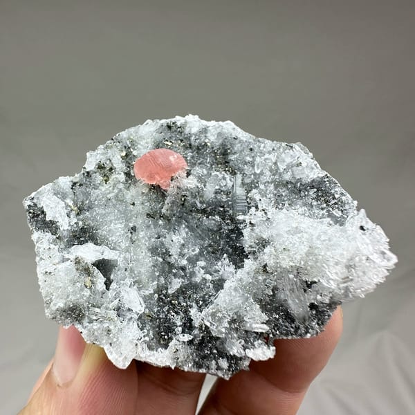 Pink rhodochrosite patch on dark quartz-and-pyrite plate from Guangxi, China, held in hand