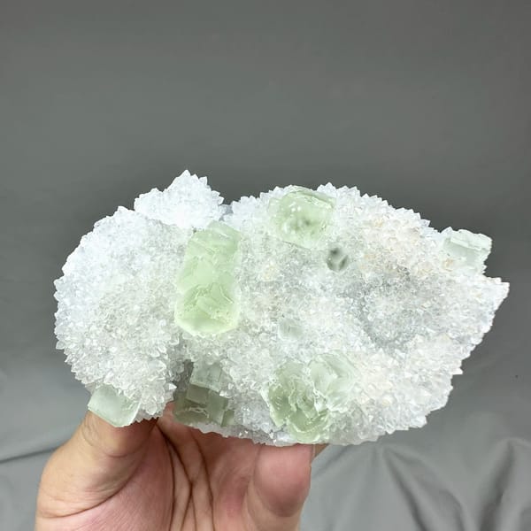Transparent pale-green fluorite cubes on frosted white quartz from Guangdong, China, held in hand