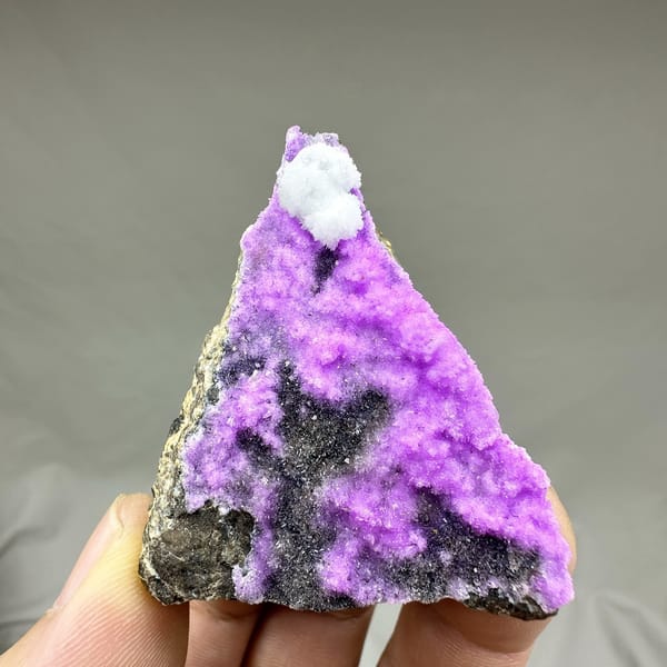 Vivid violet aragonite with white tuft on dark rock from Yunnan, China, detail of the matrix contact