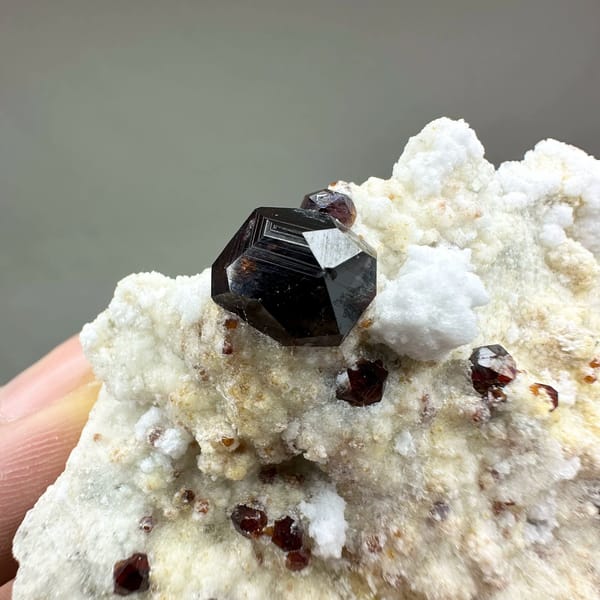 Large dark garnets with hyalite opal on cream feldspar from Yunxiao, Fujian, China, close-up of the crystal faces