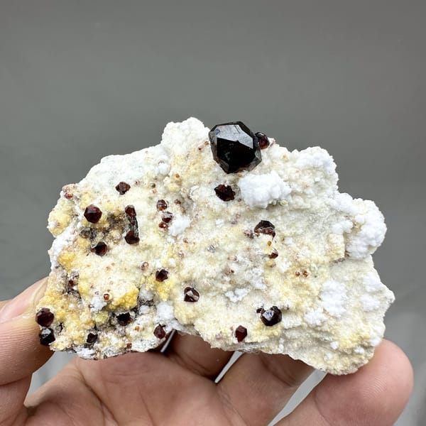 Large dark garnets with hyalite opal on cream feldspar from Yunxiao, Fujian, China, detail of the matrix contact