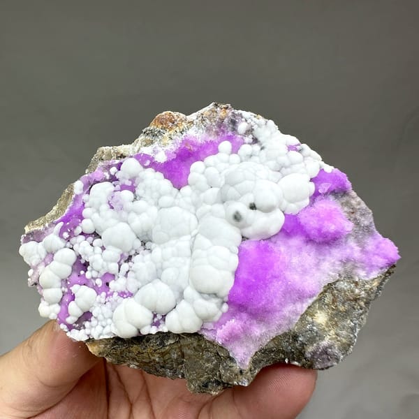 White aragonite balls in field of violet aragonite from Yunnan, China, held in hand
