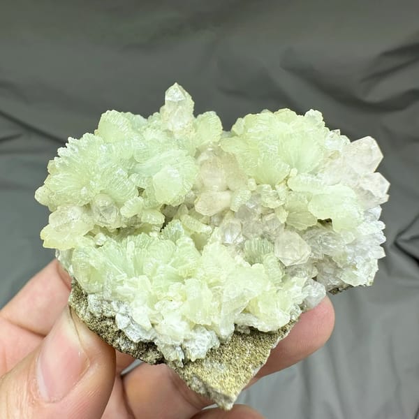 Pale green fan-shaped prehnite with quartz points from Morocco, held in hand
