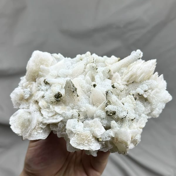 Plate of frosted white calcite crystals with pyrite from Fujian, China, held in hand
