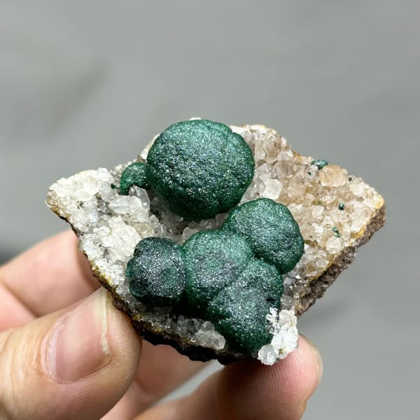 Three large velvet-green malachite balls on white quartz from DR Congo, held in hand