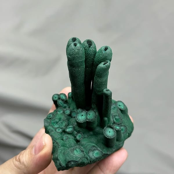 Dark green malachite stalactite pillars from DR Congo, held in hand