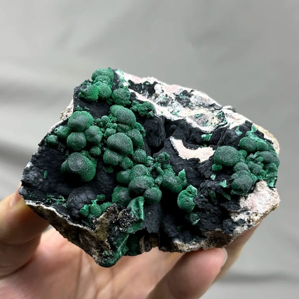 Green malachite balls over black manganese oxide from DR Congo, held in hand