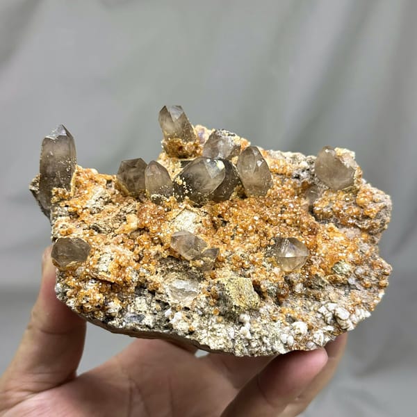 Smoky quartz points over Fanta-orange garnet druse from Yunxiao, Fujian, China, detail of the matrix contact