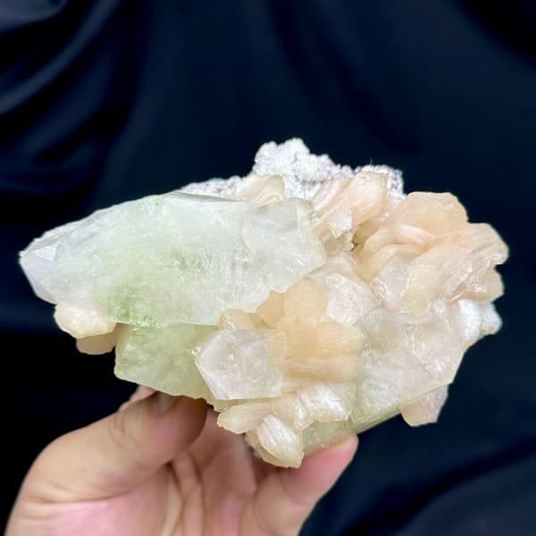 Large pale-green apophyllite crystal with peach stilbite from India, held in hand