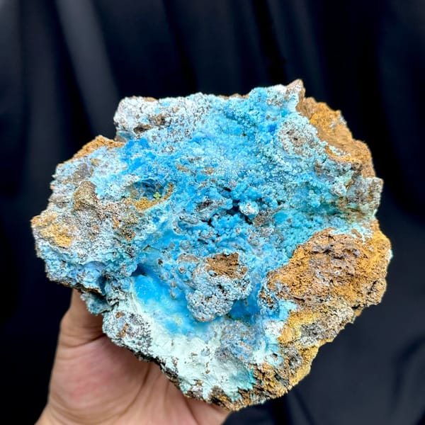 Electric-blue allophane crust in rusty rock pocket from Yunnan, China, held in hand
