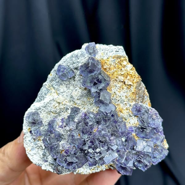 Blue-green phantom fluorite cubes on tan-stained plate from Fujian, China, held in hand