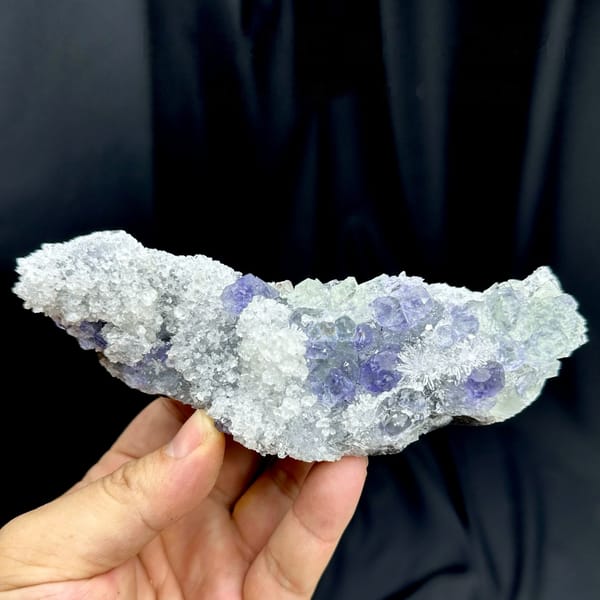 Long bar of sparkling quartz with violet-blue fluorite from Fujian, China, held in hand