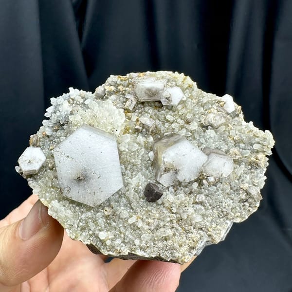 Hexagonal sandwich calcite plates with limonite on grey druse from Fujian, China, held in hand