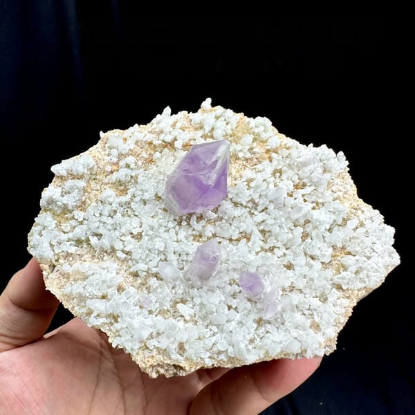 Pale amethyst point standing on white feldspar plate from Yunxiao, Fujian, China, held in hand
