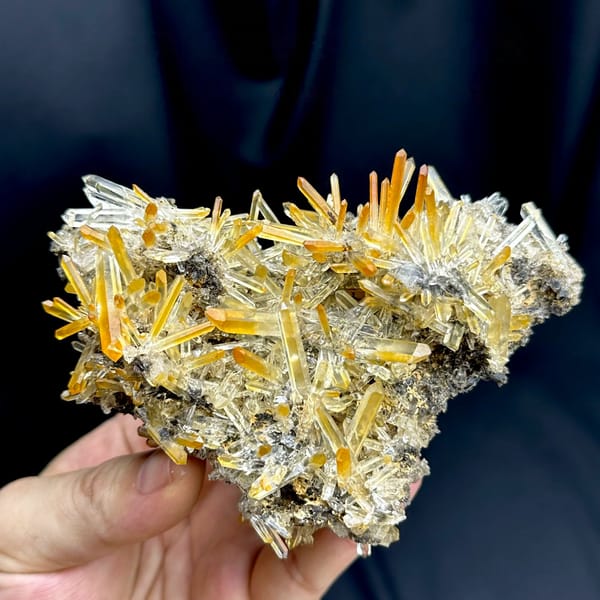 Cluster of clear quartz needles with mango-orange tips from Jinkouhe, Sichuan, China, held in hand