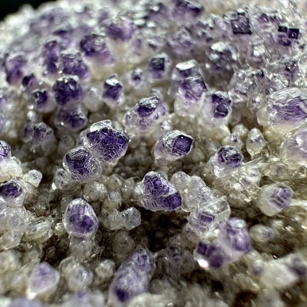Purple yttrofluorite balls on white gypsum mound from Guizhou, China, close-up of the crystal faces