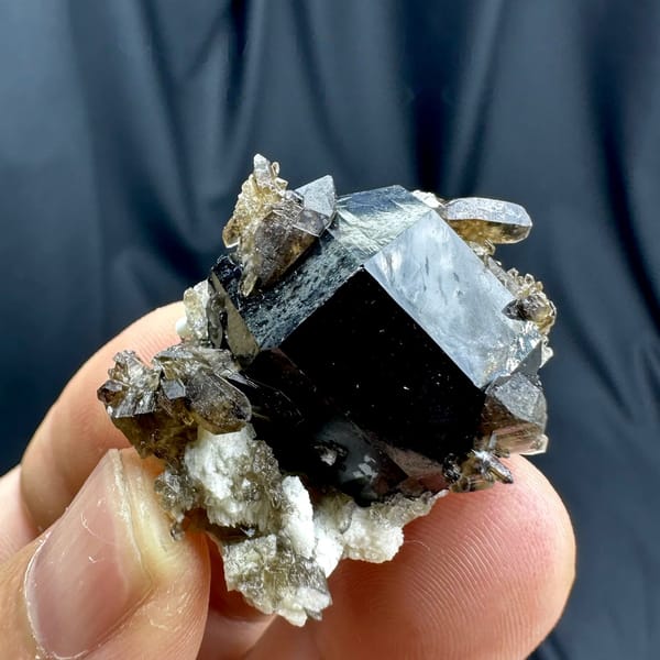 Jet-black tourmaline crystal with smoky quartz and feldspar from Namibia, held in hand