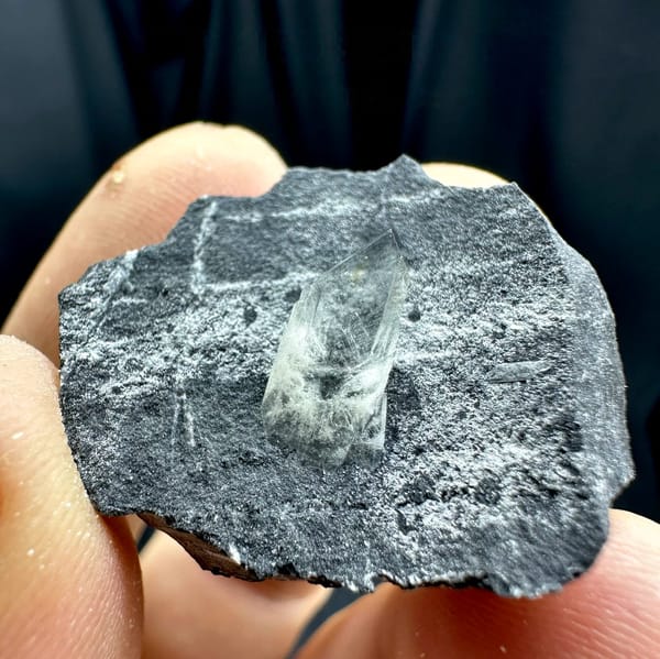 Sword-tip transparent baryte blade on dark grey rock from Guangxi, China, held in hand