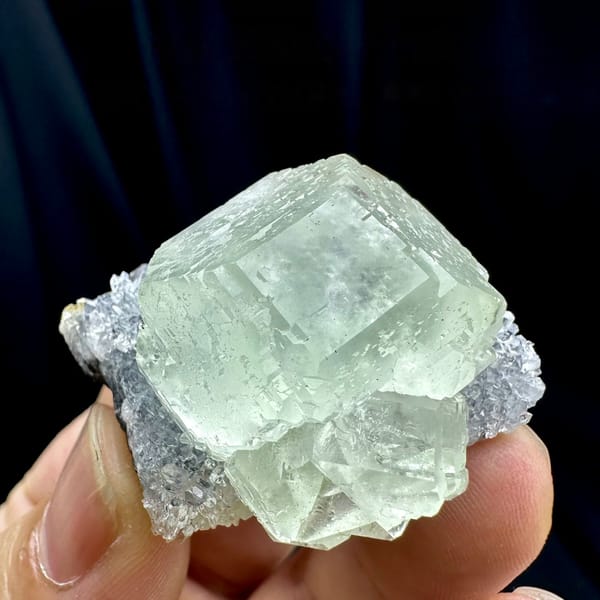 Large glass-clear pale green fluorite cube on lavender druse from Fujian, China, held in hand